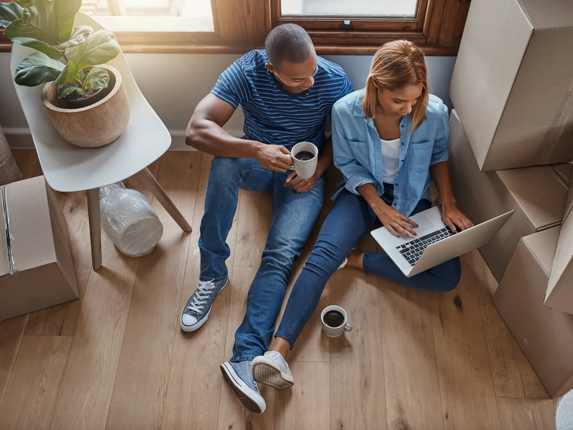 A couple sitting among moving boxes, reviewing their mortgage options together on a laptop