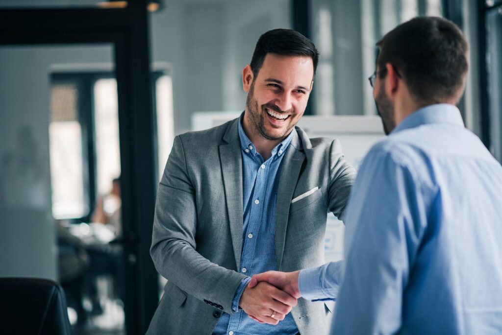 Two people shaking hands across a desk after reaching an agreement