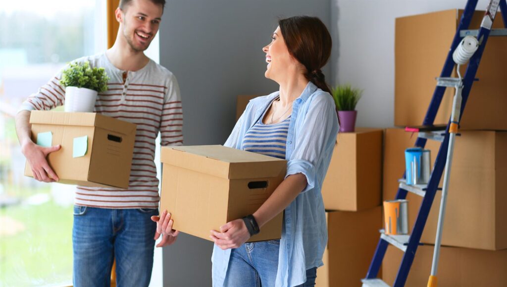 A couple carrying moving boxes into a home