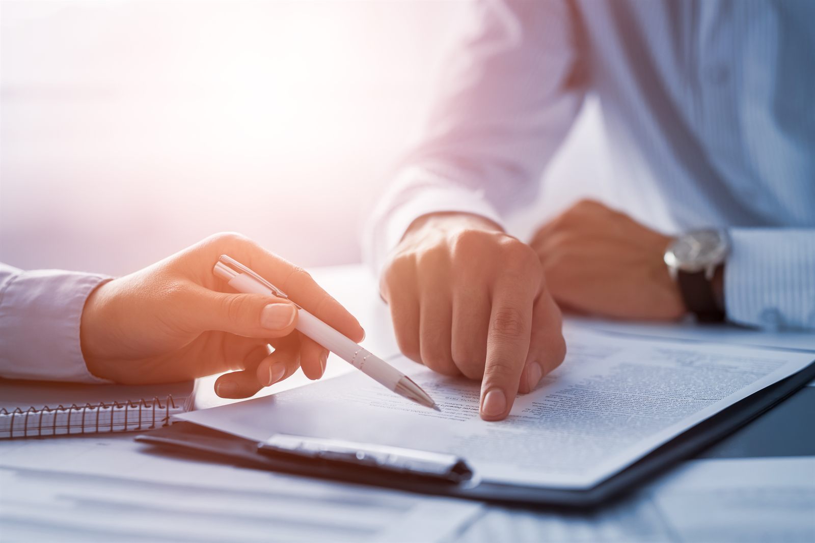 Hands signing a contract at a desk covered with loan documents