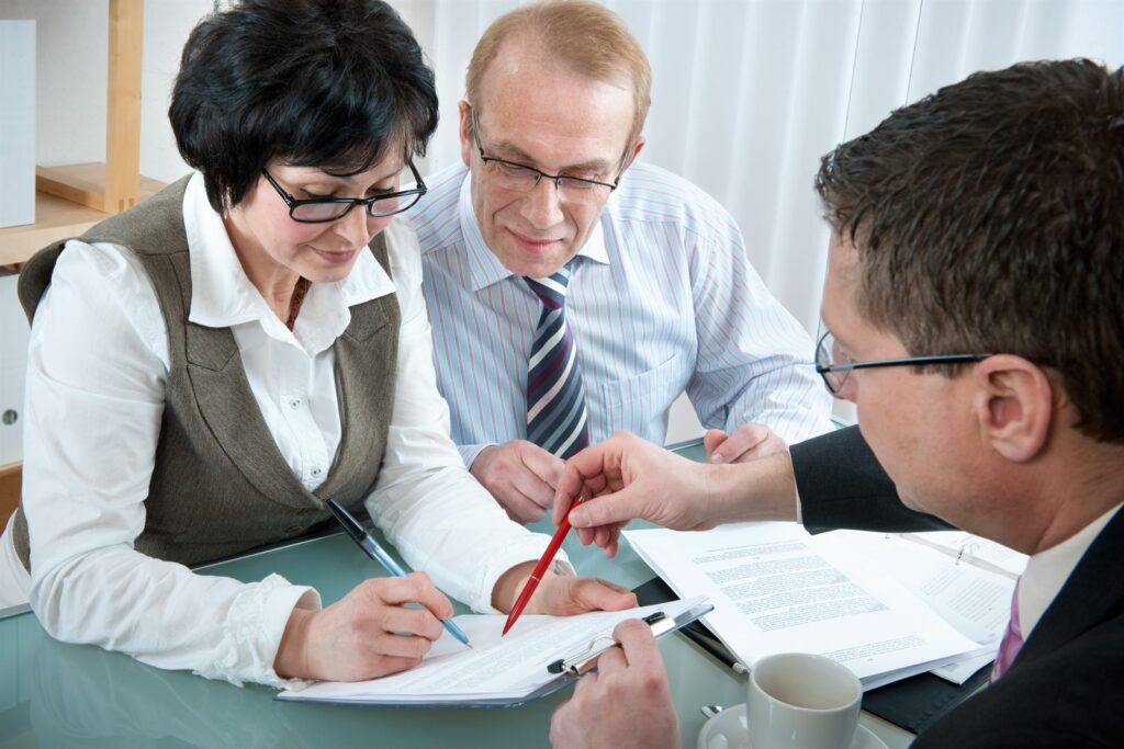 A couple signing documents while an advisor points to a clause on the contract