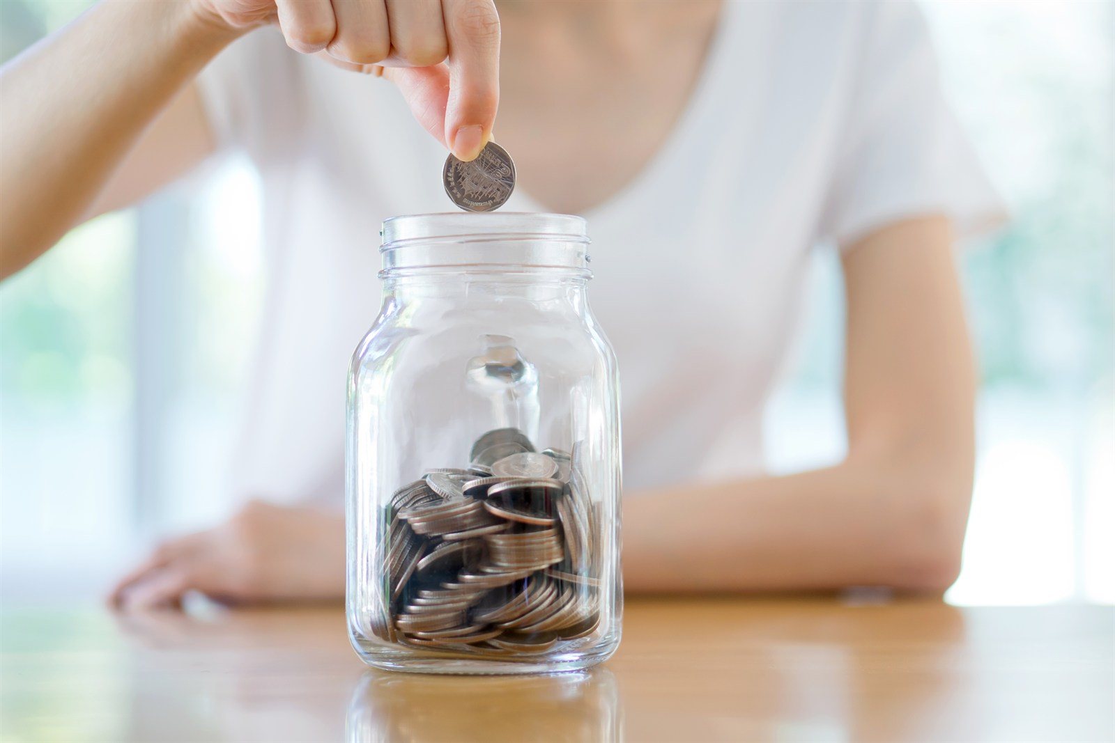 A hand dropping a coin into a jar of savings