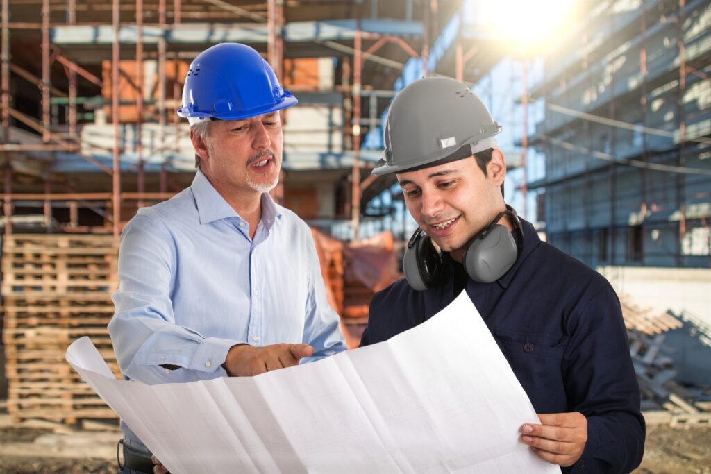 Two engineers in hard hats reviewing plans at a construction site