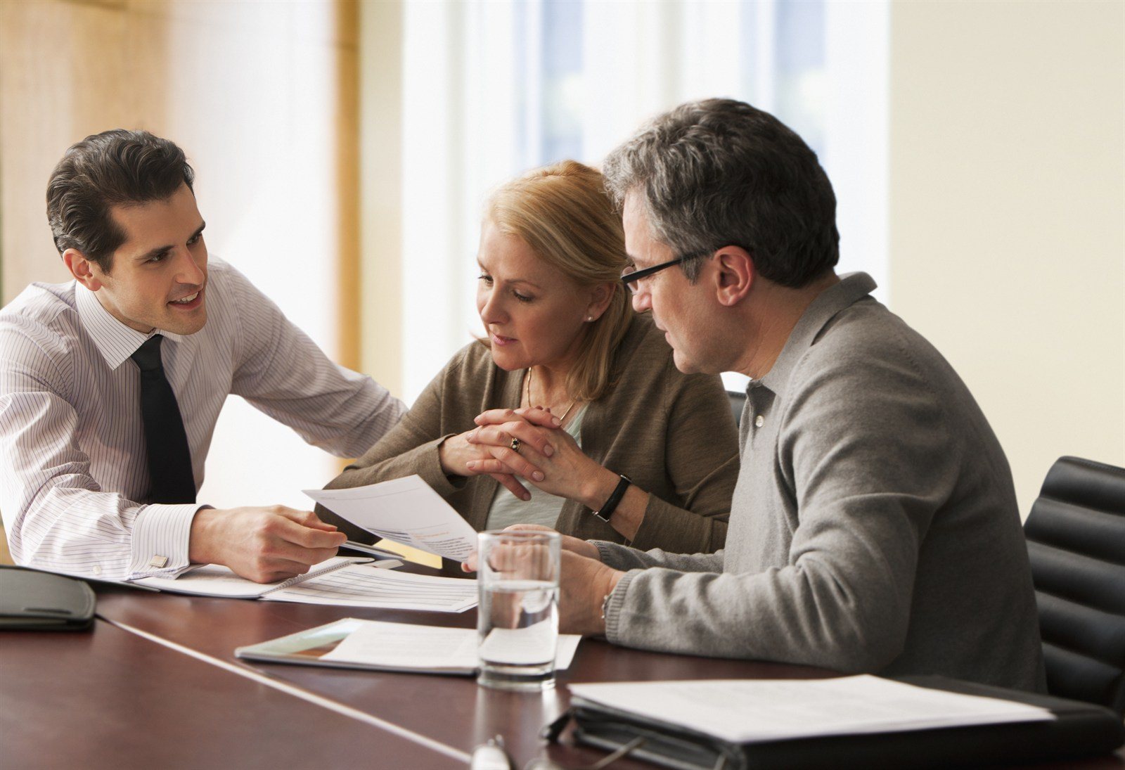 Three people reviewing documents together at a boardroom table