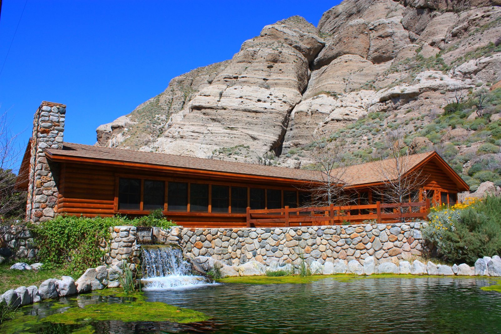 Timber lodge home set below red rock cliffs beside a pond