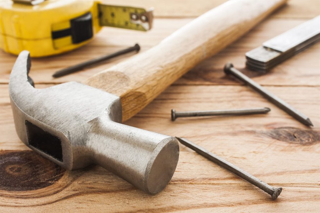 A hammer, nails and a tape measure on a wooden workbench