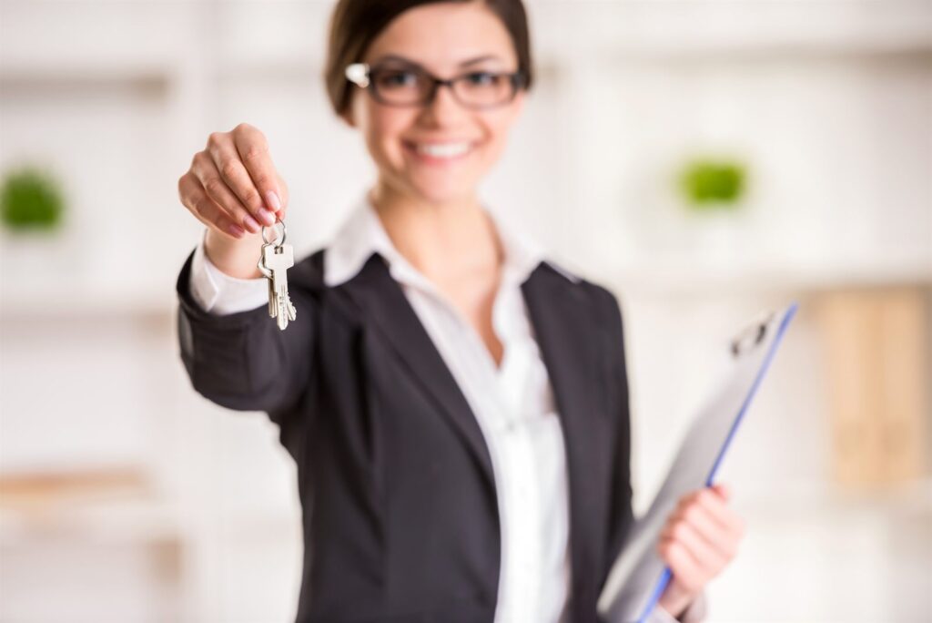 An agent handing over house keys while holding a clipboard