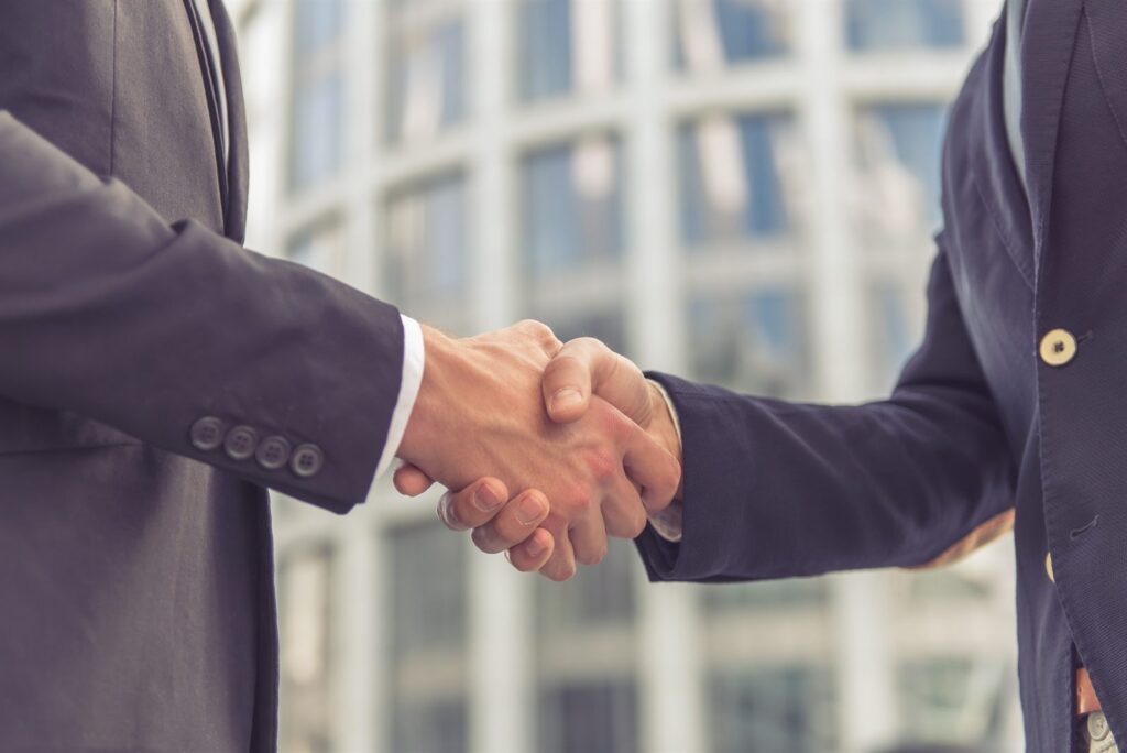 Two people shaking hands in front of a glass office building