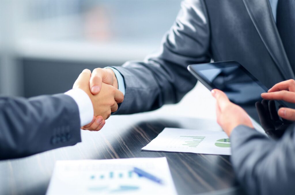 Two people shaking hands across a desk over loan documents