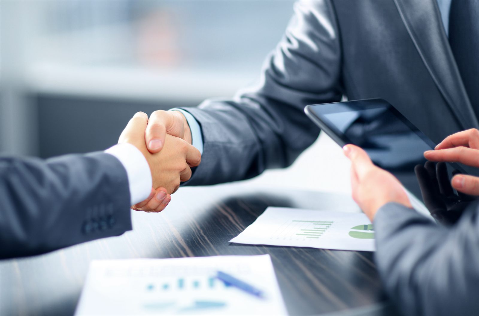 Two people shaking hands across a desk over loan documents