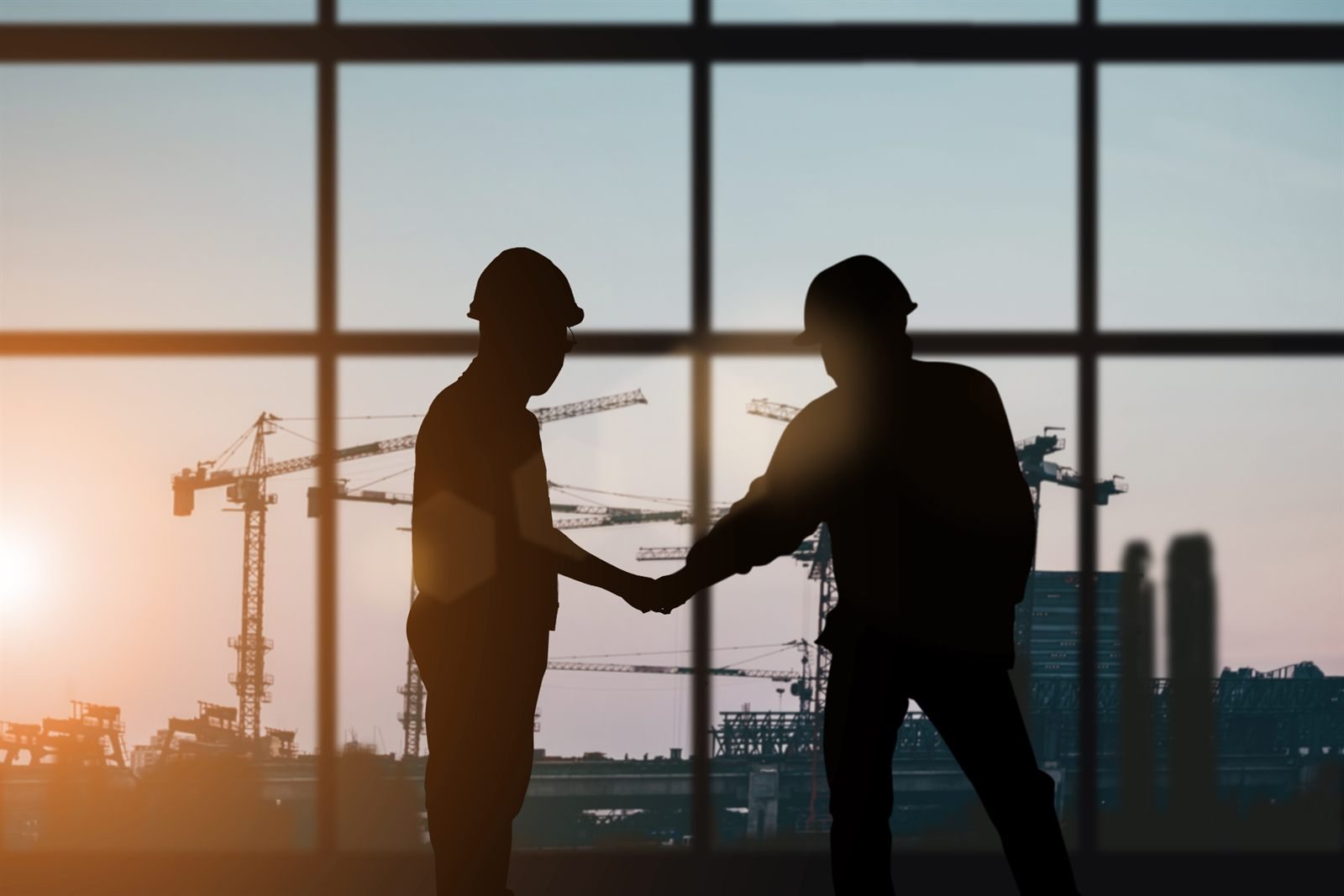 Two people shaking hands at a construction site at dusk