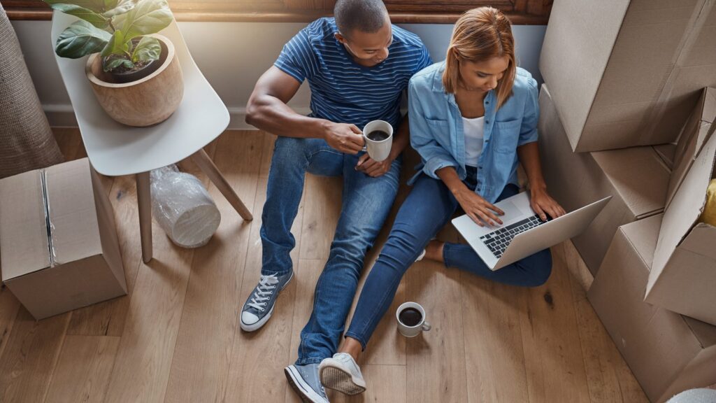 A couple sitting among moving boxes reviewing mortgage options on a laptop