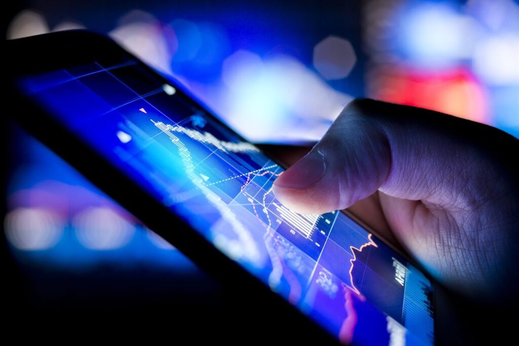 Finger touching a tablet screen showing financial charts