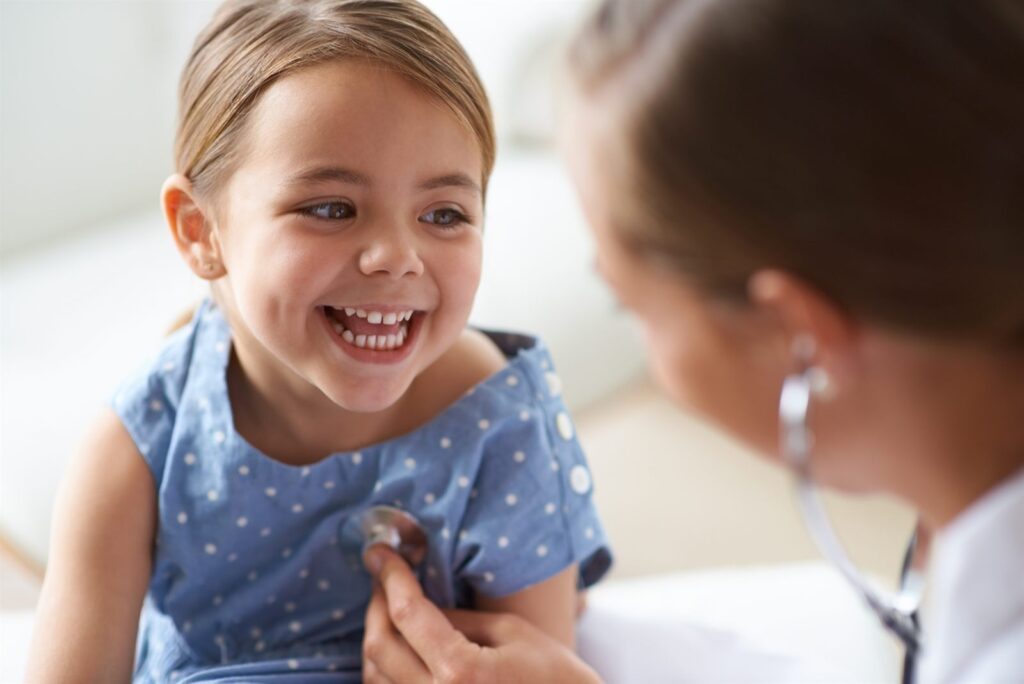A pediatrician examining a smiling young child with a stethoscope