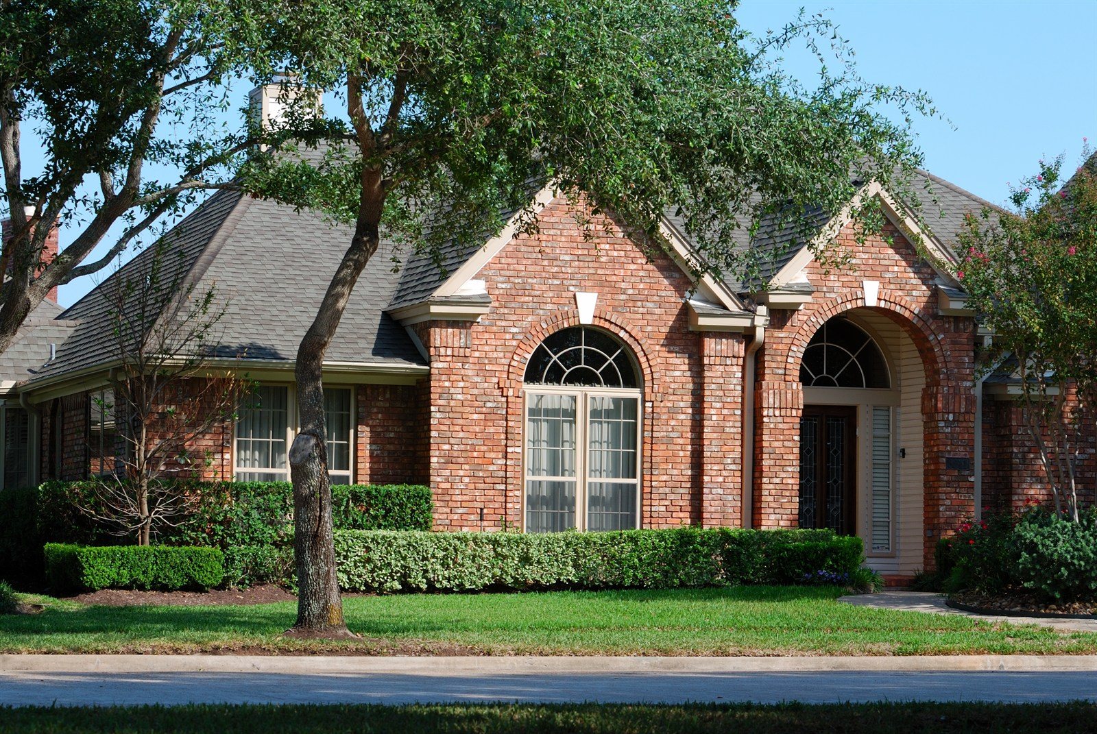 A single storey brick home with a mature tree and lawn